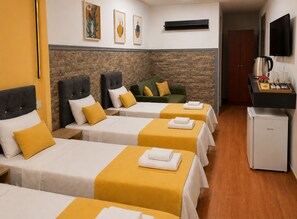 A hotel room with three beds, a sofa, a coffee machine, and a TV.