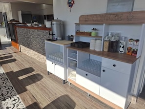 A coffee station with a wooden sign, shelves with cups and milk cartons, and a kitchen area in the background. - Hotel Efesian B&B City Center - Harbour (Kuşadası)