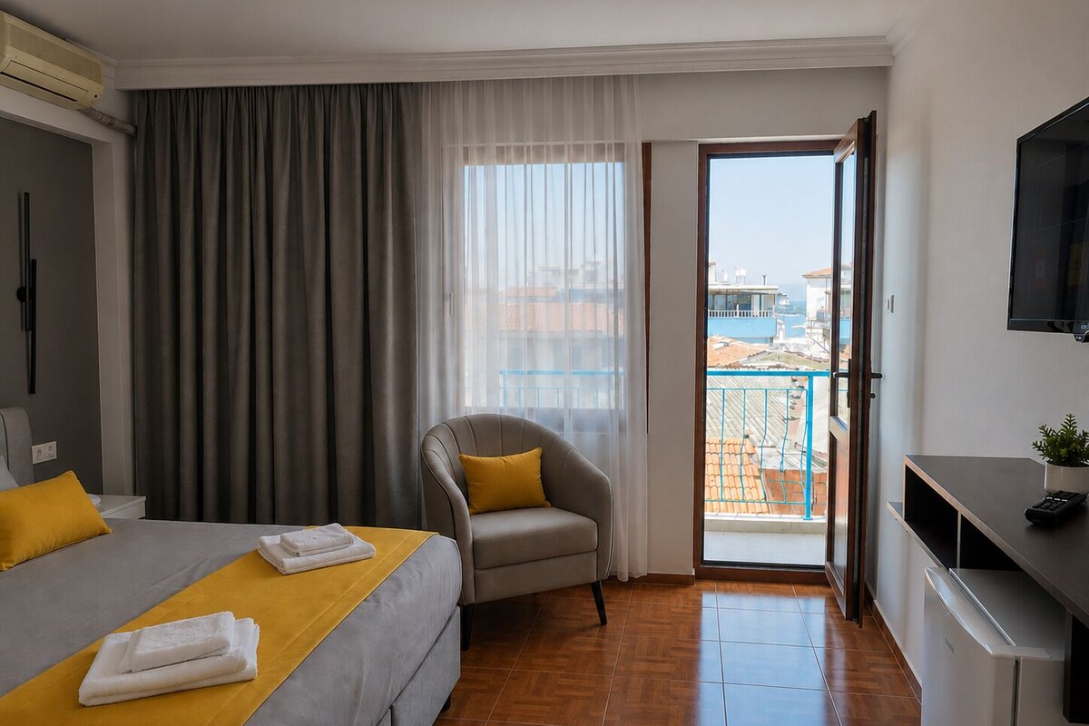 A hotel room with a bed, a chair, a desk, a TV, and a balcony with a view.