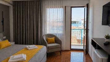 Een hotelkamer met een bed, een stoel, een bureau, een televisie en een balkon met uitzicht.