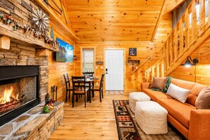 Un interior de cabaña acogedor, con chimenea de piedra, mesa de comedor de madera y sofá.