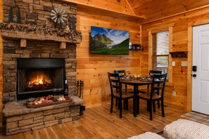A cozy cabin interior with a stone fireplace, a dining table with chairs, and a painting of a mountain landscape. - Mtn Cabin Hot Tub & Fireplace (Sevierville)