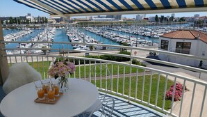 Ein Balkon mit Blick auf einen Hafen voller Boote, einem Tisch mit Getränken und einer Blumenvase.