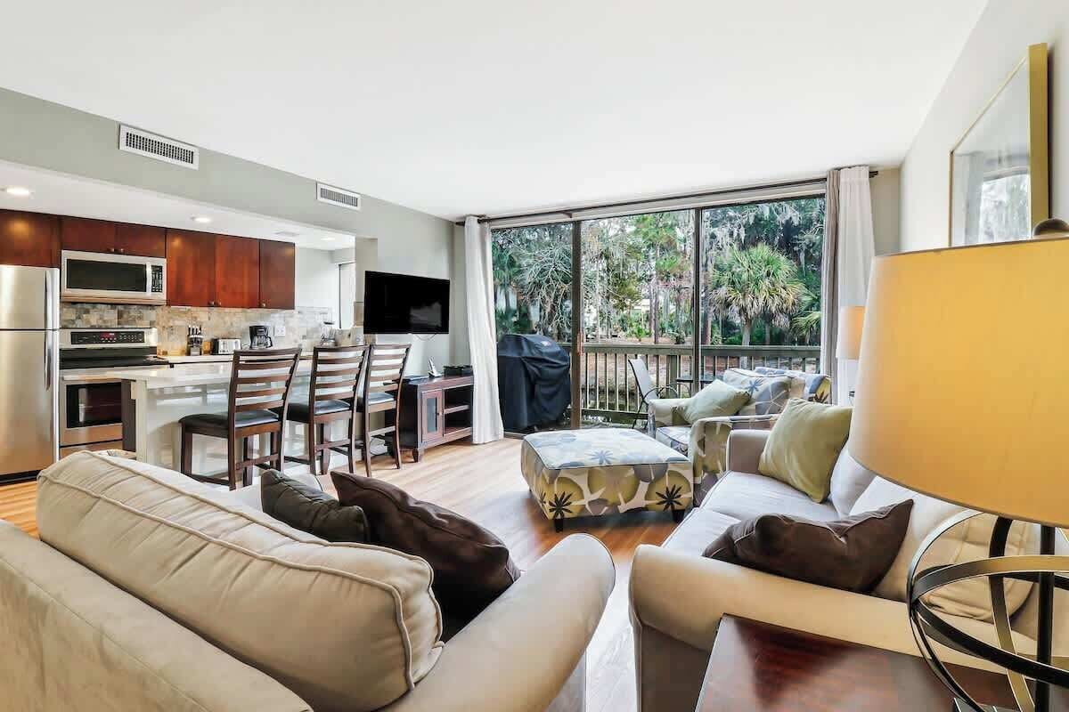 A modern living room with a sofa, ottoman, and a dining area with chairs and a table.