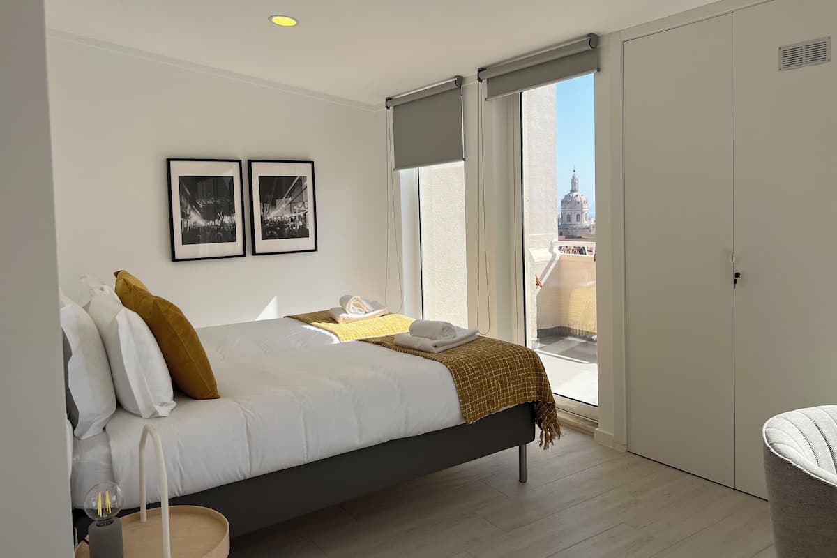 A modern bedroom with a bed, a bedside table, a lamp, and a window with a city view.