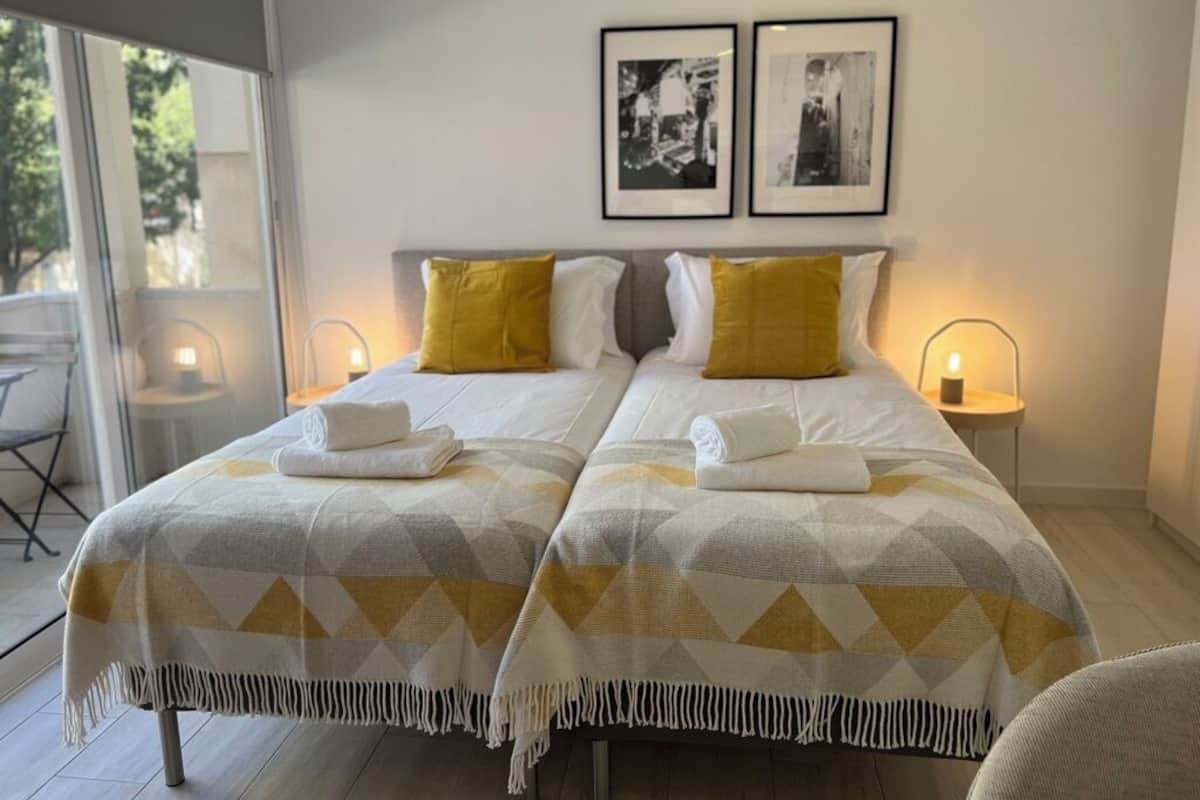 A double room with two beds, each with a patterned bedspread, yellow pillows, and a pair of framed pictures on the wall.
