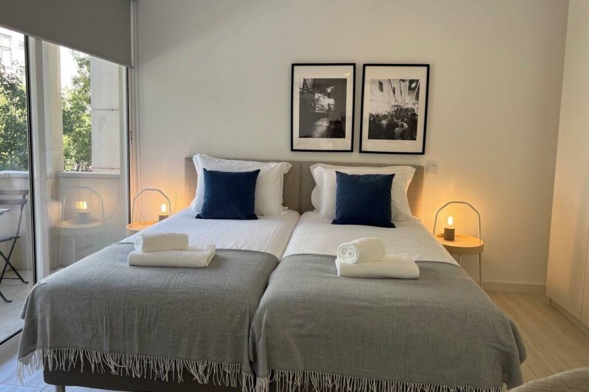 A double bed with two pillows, a bedside table with a lamp, and two framed pictures on the wall.