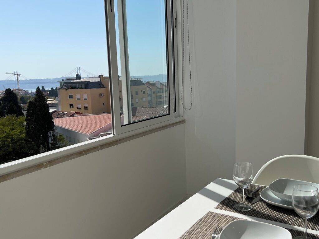 Un balcón con una mesa dispuesta para dos personas, con vistas a un paisaje urbano que incluye edificios y un puente.
