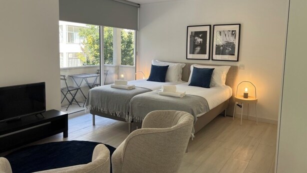 Ein modernes Hotelzimmer mit einem Bett, zwei Sesseln, einem Fernseher und einem Balkon mit Tisch und Stühlen.