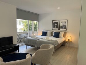 Une chambre d’hôtel moderne équipée d’un lit, de deux fauteuils, d’une télévision et d’un balcon avec une table et des chaises.