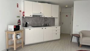 Eine kleine Küche mit weißen Schränken, einer Mikrowelle, einer Kaffeemaschine und einem Toaster auf einem Holzwagen.