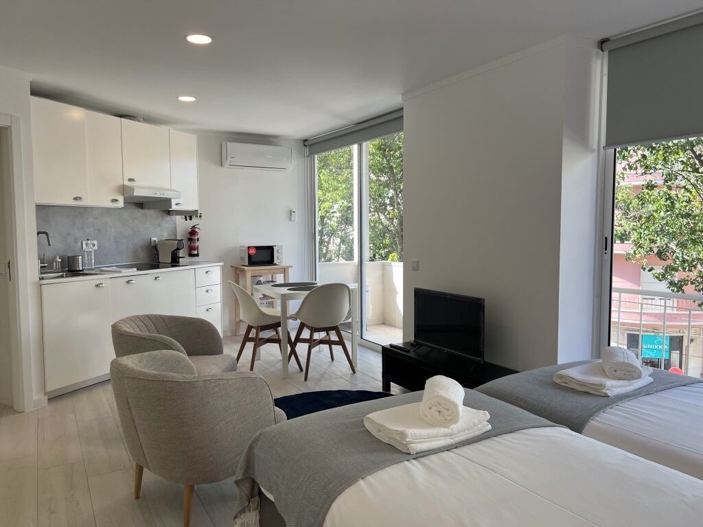 A modern hotel room with a kitchenette, a dining area, a TV, and two beds.