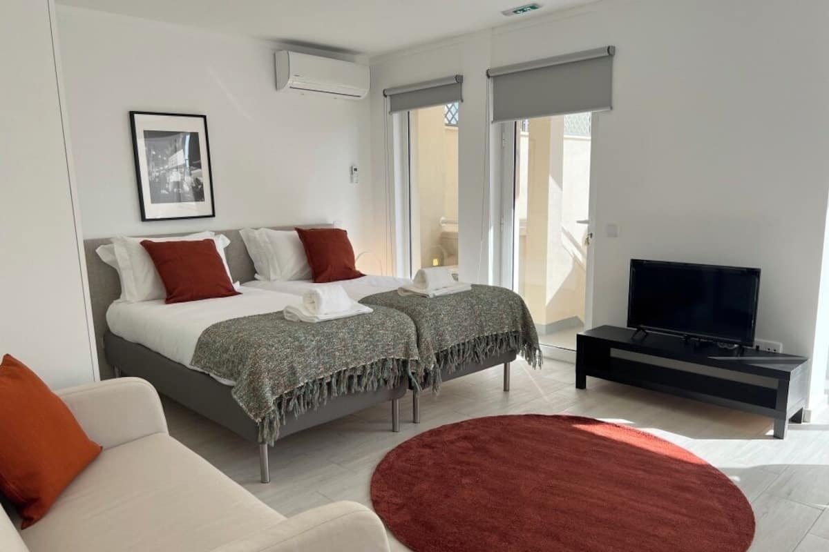 A modern bedroom with a bed, a TV, a sofa, and a red rug.