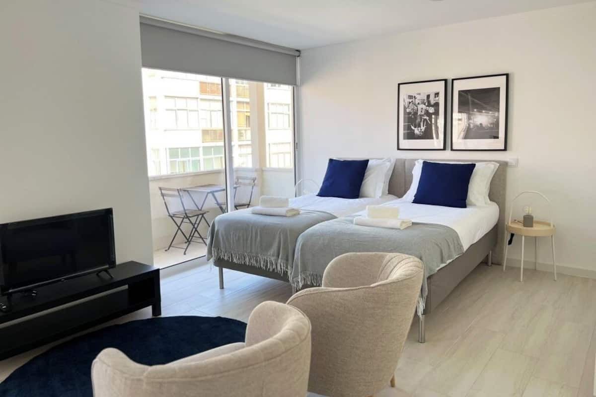 A hotel room with a bed, two chairs, a TV, and a balcony with a table and chairs.