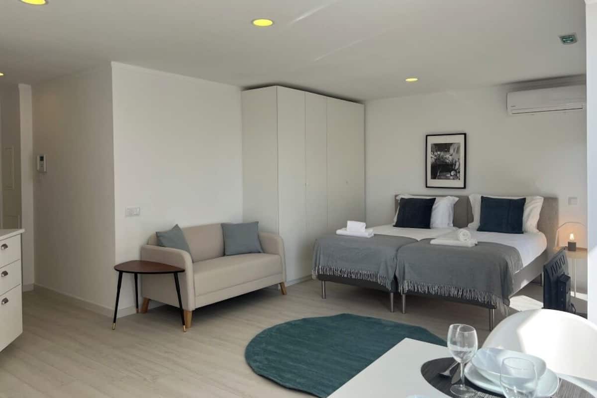 A modern hotel room with a bed, a sofa, a small table, and a desk.