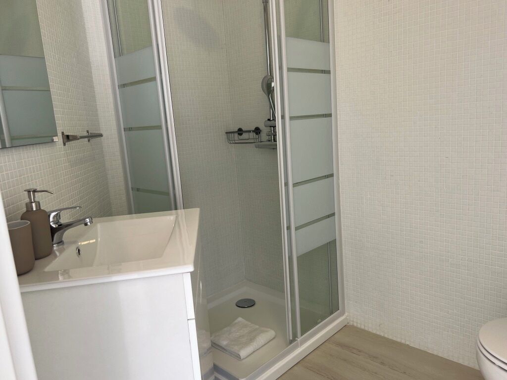 Ett modernt badrum med en duschavdelning med glasväggar, en vit tvättställ med en beige bänkskiva och en spegel ovanför tvättstället.