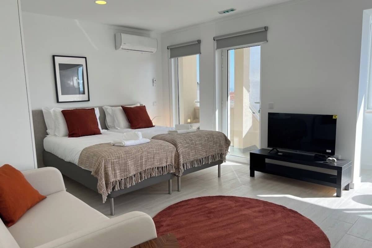 A modern hotel room with a bed, a TV, and a balcony with large windows.