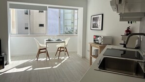 Eine moderne Küche mit großem Fenster, einer Essecke mit zwei Stühlen und einer Mikrowelle auf einem kleinen Tisch.