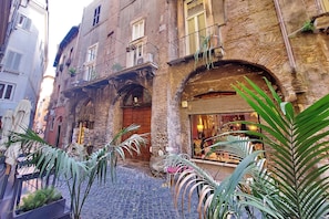 A narrow cobblestone street with a building featuring a wooden door, balconies with plants, and a shop with glass display. - Piazza Navona Hydromassage Tub 7 people (Rome)