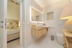 A modern bathroom with a wooden vanity, a large mirror, a toilet, and a bedside table with a bed in the adjacent room. - Piazza Navona Hydromassage Tub 7 people (Rome)