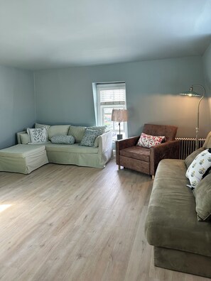 Un salon avec un canapé d’angle, un fauteuil marron et une lampe sur pied.