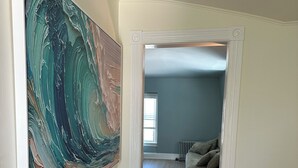 Un pasillo con un cuadro abstracto grande, suelo de madera, un radiador y un sofá al fondo.