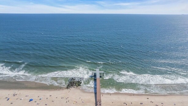 Una playa con un muelle que se adentra en el océano, arena y cielo azul despejado.