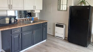 Una cocina con armarios blancos, un refrigerador negro, un microondas y un fregadero.
