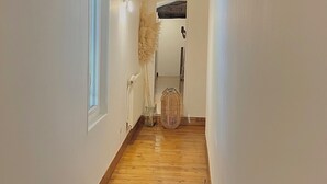 Un pasillo estrecho con suelo de madera, paredes blancas y techo con vigas de madera oscura.