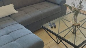 Una sala de estar con un sofá gris, una mesa de centro de vidrio y una puerta al fondo.