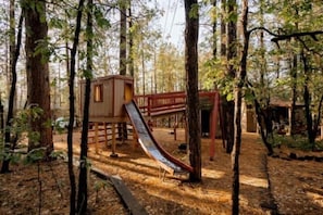 Un parque infantil con un tobogán y una casita de madera en un área boscosa.