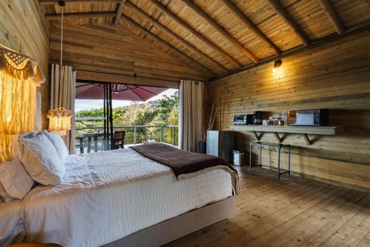 A wooden cabin bedroom with a bed, a small table, and a kitchenette.
