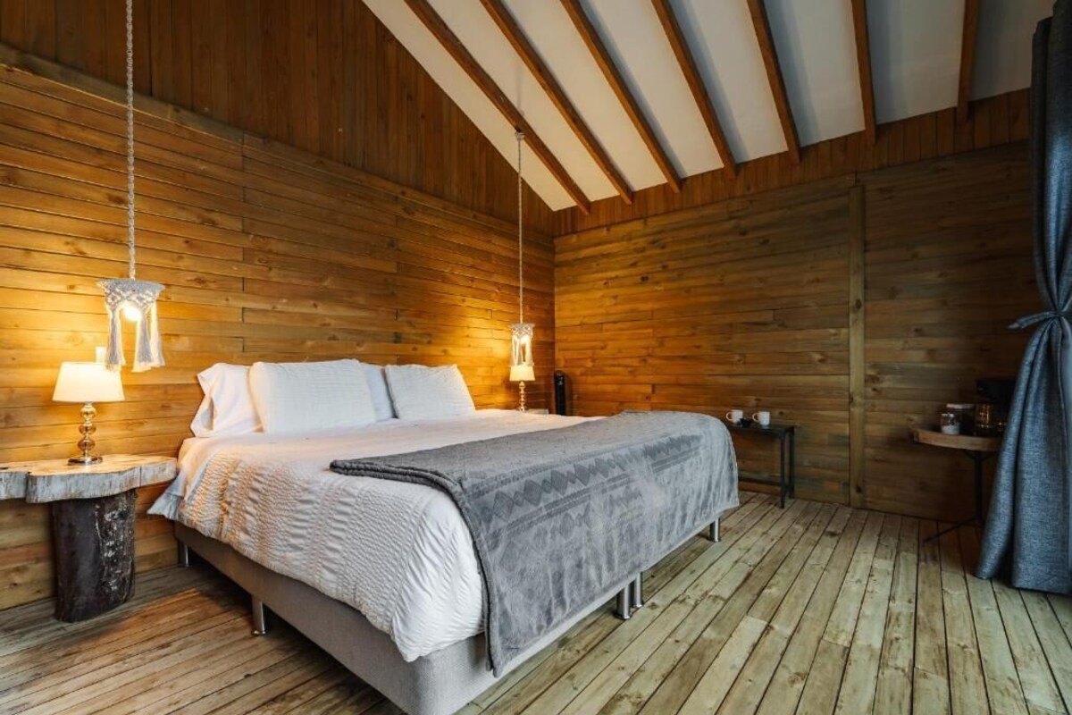 A wooden-paneled room with a bed, two bedside lamps, and a small table with a lamp.