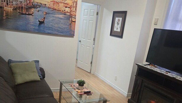 A living room with a leather sofa, a glass coffee table, a fireplace, and a large cityscape painting on the wall.