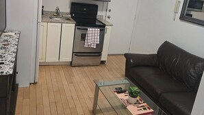 A compact living space with a kitchenette, a glass coffee table, a black leather sofa, and a mirror on the wall.