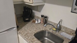 A compact kitchen with white cabinets, a stainless steel sink, a black stove, and a granite countertop.
