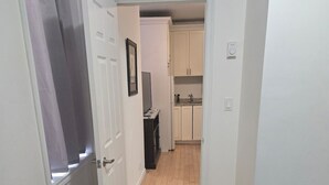 A narrow hallway leading to a kitchen with cabinets and a small table.