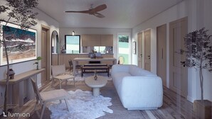 A modern living room with a white sofa, a dining table, and a kitchen area with wooden cabinets and a large window. - The Goldenrod - Catskills Mountain Retreat (Parksville)