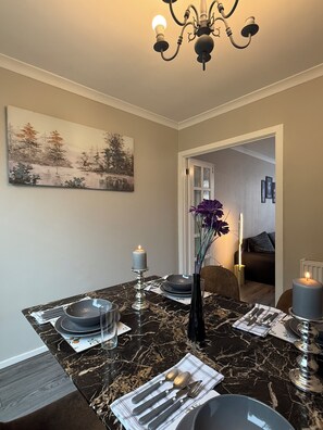 Un comedor con una mesa de mármol, velas, un florero con flores y un cuadro en la pared.