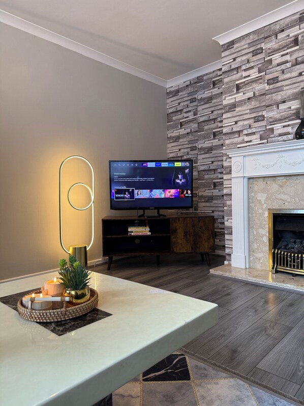 Una sala de estar moderna con un televisor de pantalla plana sobre un soporte de madera, una chimenea y una pared decorativa con un diseño geométrico.