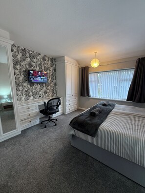 Un dormitorio con cama, escritorio, silla, televisor y ventana con cortinas.