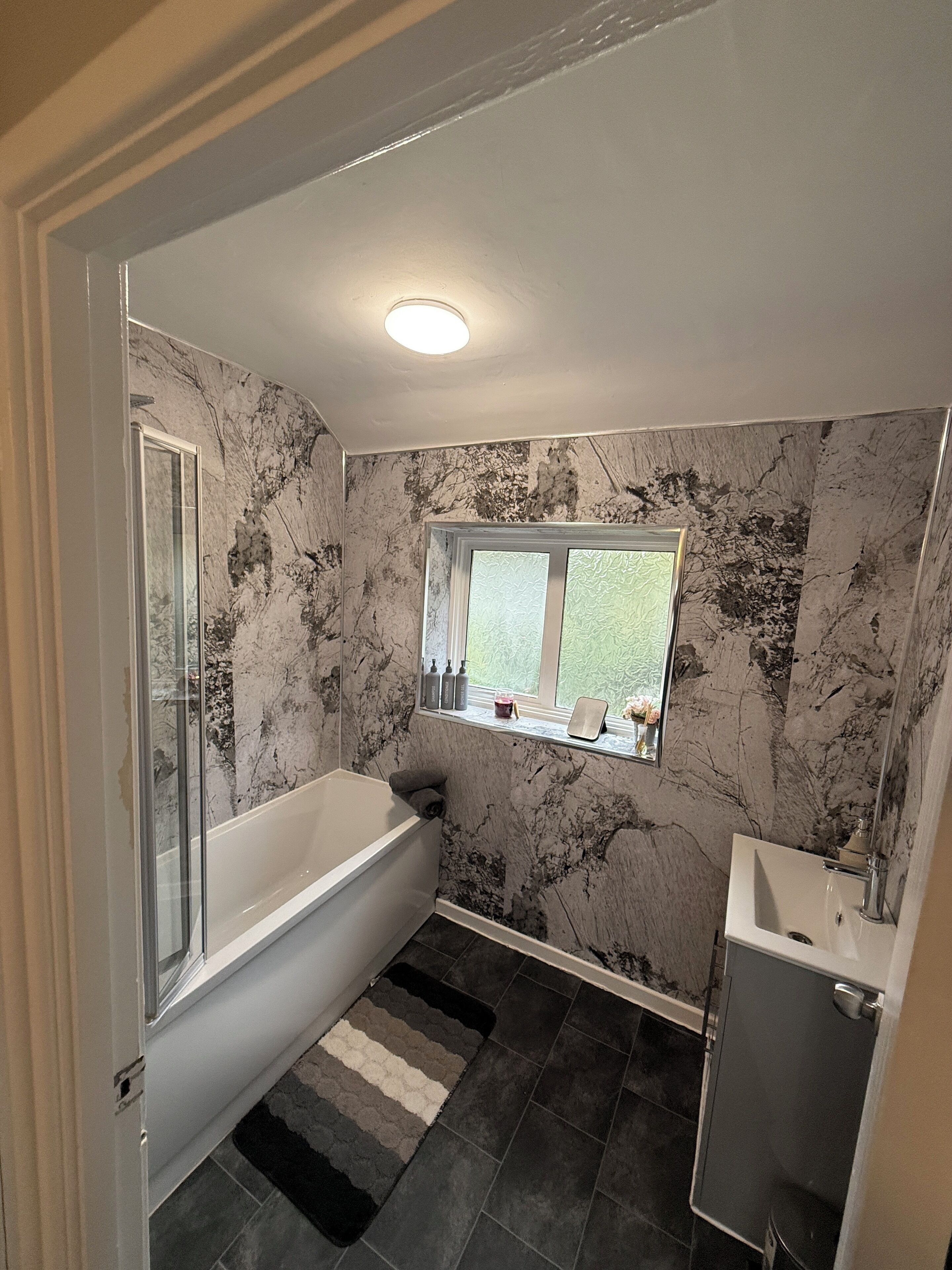 A bathroom with a bathtub, a window, a sink, and a shower.