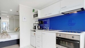 A modern kitchen with white cabinets, a blue backsplash, a microwave, a coffee maker, and a double oven. - Comfortable Studio, Aircon, Central Location (Auckland CBD)