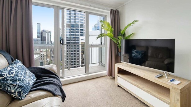 A living room with a sofa, TV, and a large window with a city view. - Comfortable Studio, Aircon, Central Location (Auckland CBD)