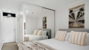 A bedroom with a large bed, a mirror, and a painting of palm trees. - Comfortable Studio, Aircon, Central Location (Auckland CBD)