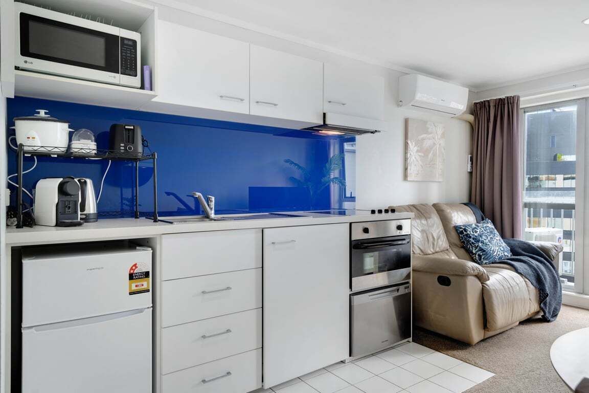 A compact kitchen with a microwave, toaster, and coffee maker, a sofa with a massage chair, and a large window.
