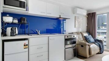 A compact kitchen with a microwave, toaster, and coffee maker, a sofa with a massage chair, and a large window.