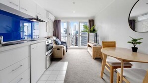 A modern kitchen with white cabinets, a blue backsplash, and a large window offering a city view. - Comfortable Studio, Aircon, Central Location (Auckland CBD)