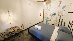 Une chambre à coucher comprenant un lit, une chaise, une table et un mur décoré d’œuvres d’art sur le thème de la mer.