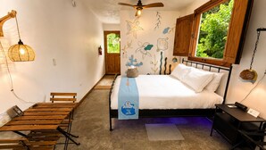 A bedroom with a bed, a wooden bench, a table, a ceiling fan, and a window with a view of greenery. - Private Finca Ki' •3BR • Hammock Terrace • El Yunque • Ceiba Ferry • Easy-Access (NAGUABO)